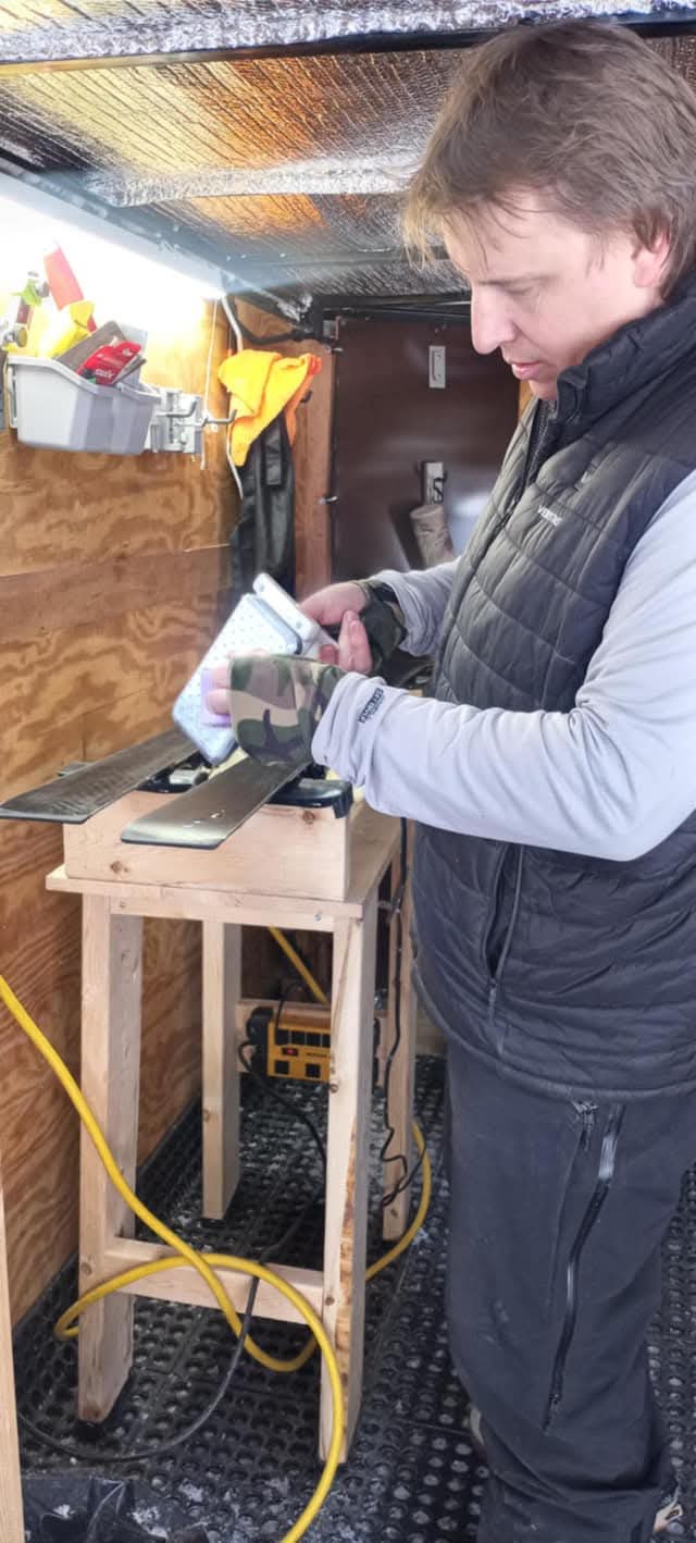 A TopSheetz tech hand-waxing a ski inside the mobile tuning trailer